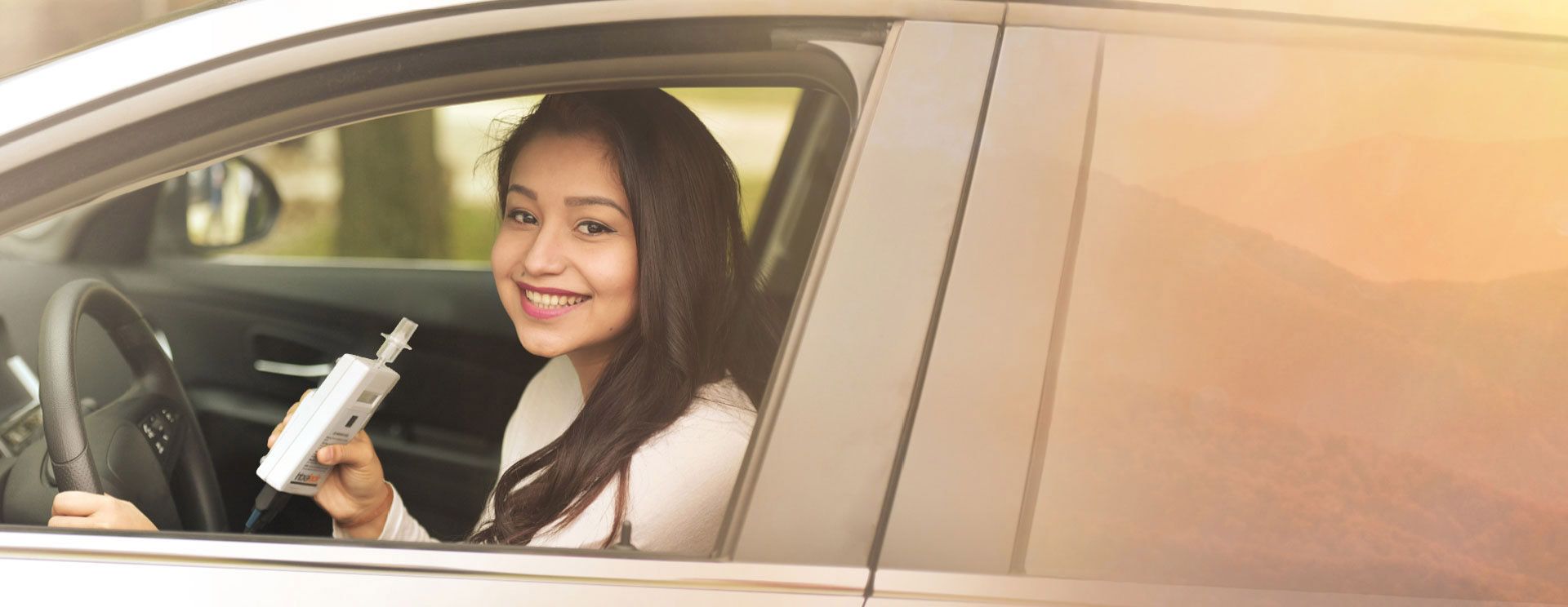 Woman in car posing with Intoxalock interlock device