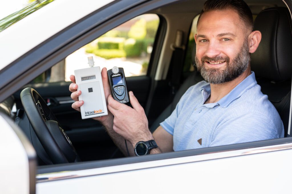 Man in car posing with an Intoxalock interlock device